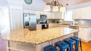 A kitchen with a granite island, stainless steel appliances, and blue bar stools.