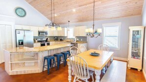 A modern kitchen with a wooden island, bar stools, and a dining table with chairs.