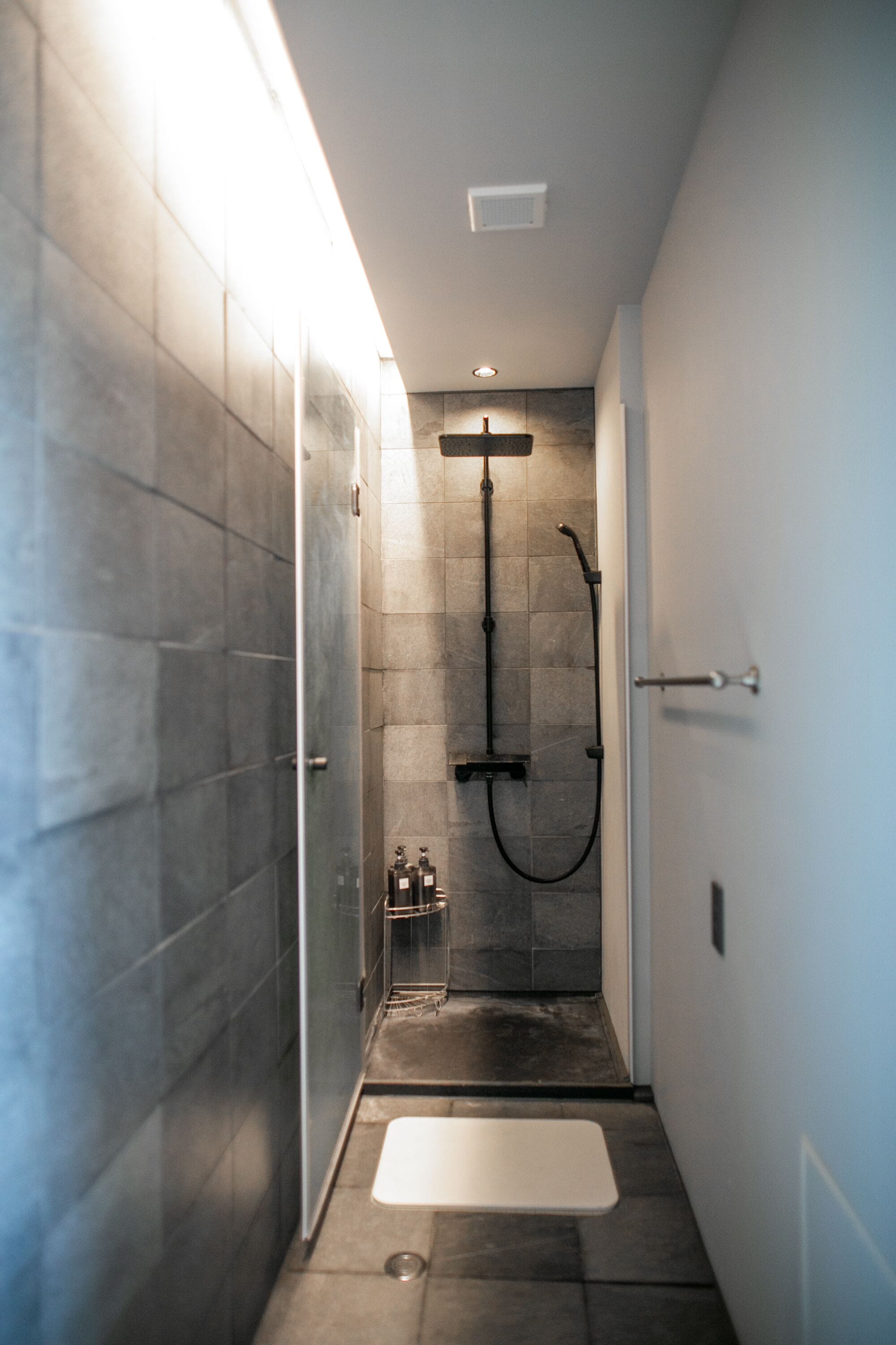 Un área de ducha moderna con puerta de vidrio, cabezal de ducha manual y panel de control empotrado.