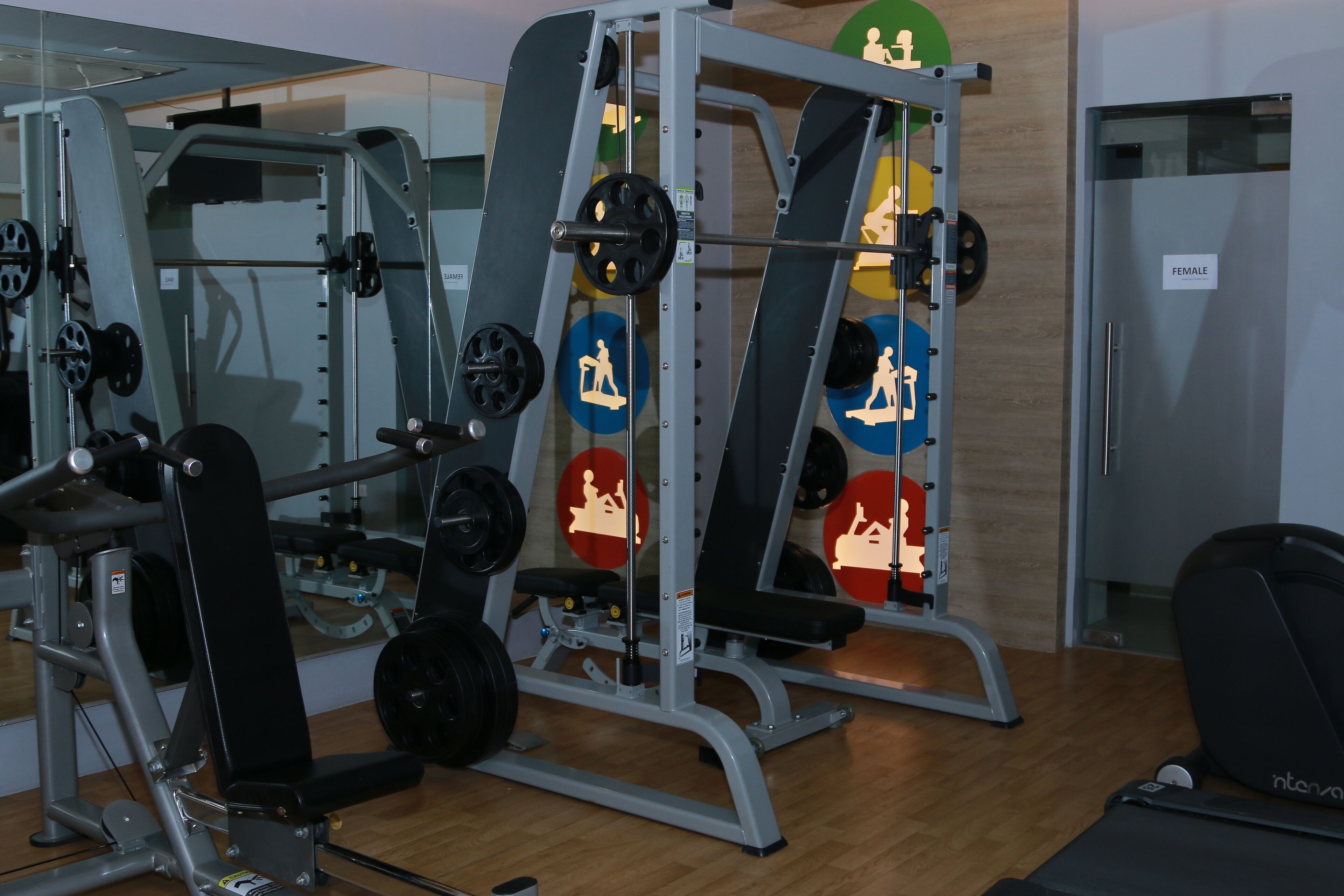 Ein Fitnessraum mit Krafttrainingsgeräten, einer Hantelbank und einem Laufband.