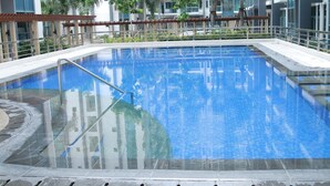 Una piscina rettangolare con scala in metallo, circondata da una terrazza piastrellata e palme.