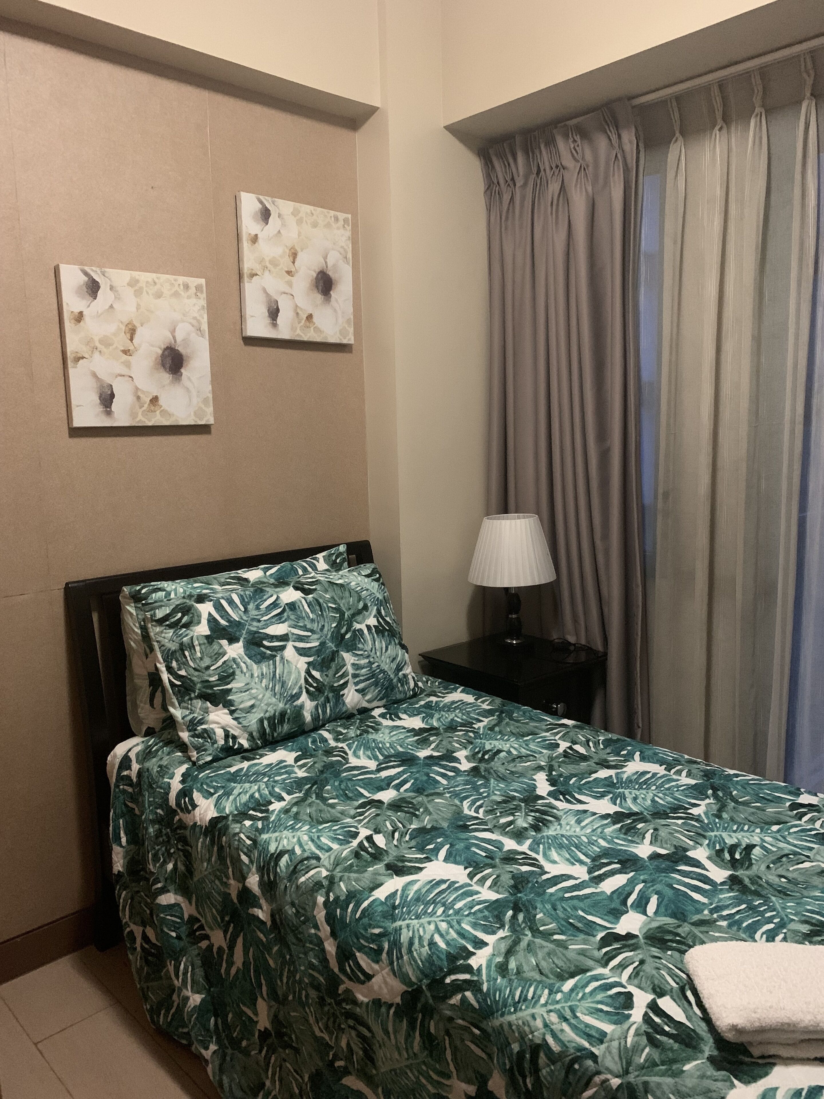 Camera d'albergo con un letto, un comodino, una lampada e due opere d'arte appese al muro.