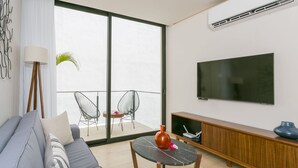 A modern living room with a sofa, a small table, a TV, and a balcony with chairs.