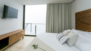 A modern hotel room with a large bed, a wooden console table, a flat-screen TV, and a balcony with a view.