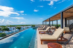 Une piscine à débordement située sur le toit, avec des chaises longues et une pergola en bois, offrant une vue sur la côte.