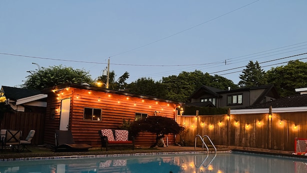 Un jardin avec une piscine, une terrasse en bois et des guirlandes lumineuses.