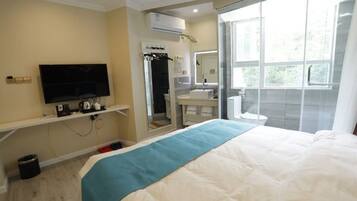 A hotel room with a bed, a TV, a bathroom with a mirror, and a window.