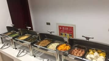A buffet line with various food items in metal containers, a door in the background, and a sign on the wall.