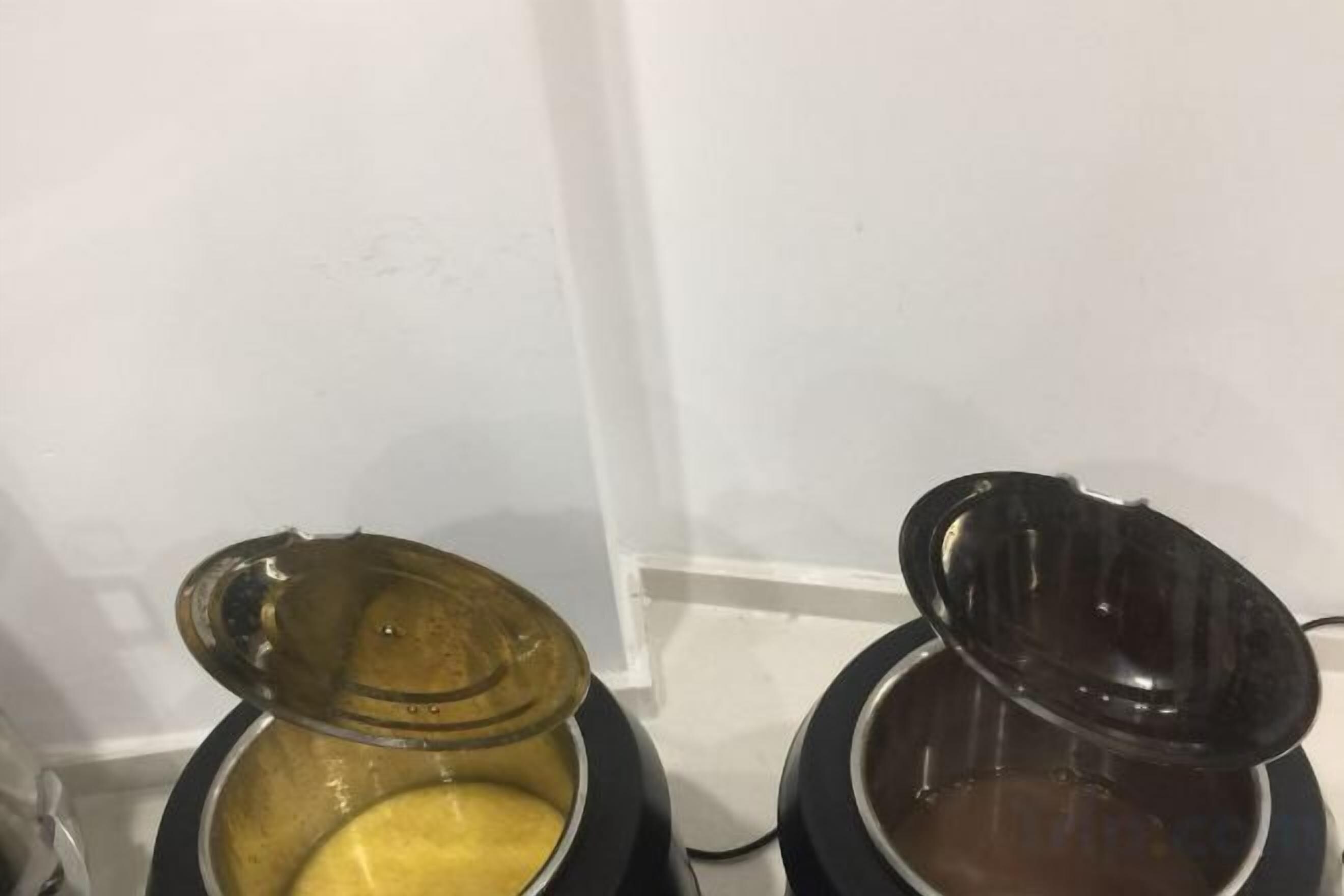 Två behållare, den ena med ett gult ämne och den andra med en brun vätska, placerade framför en vit vägg.