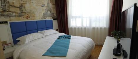 Una camera d'albergo con un letto grande, una testiera blu, una mappa appesa al muro, una scrivania con un computer e una finestra con tende.