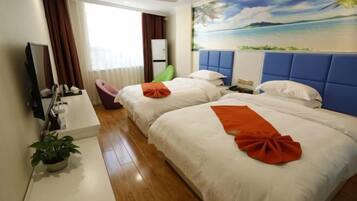 A hotel room with two beds, a large window with curtains, a painting of a beach, a potted plant, and a desk with a mirror and toiletries.