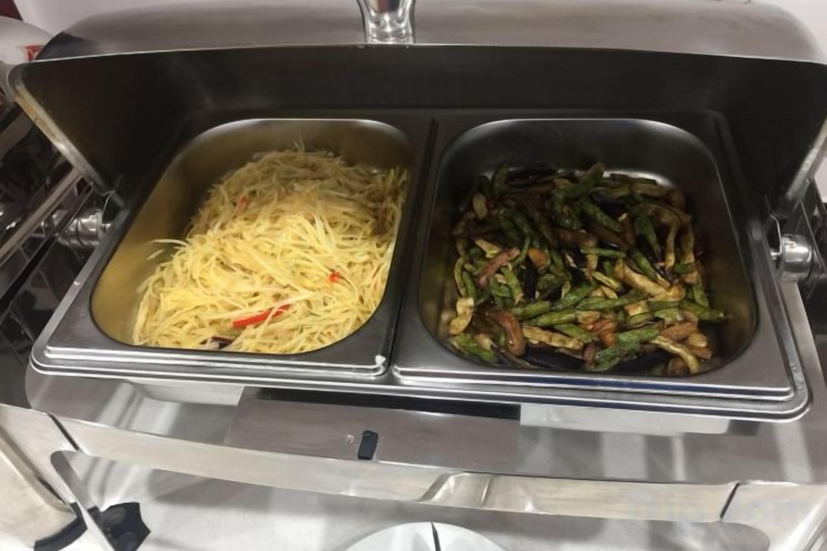 Un buffet comprenant deux plats de service en acier inoxydable, l’un contenant des spaghettis et l’autre, un plat de légumes sautés.