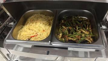 Un buffet comprenant deux plats de service en acier inoxydable, l’un contenant des spaghettis et l’autre, un plat de légumes sautés.
