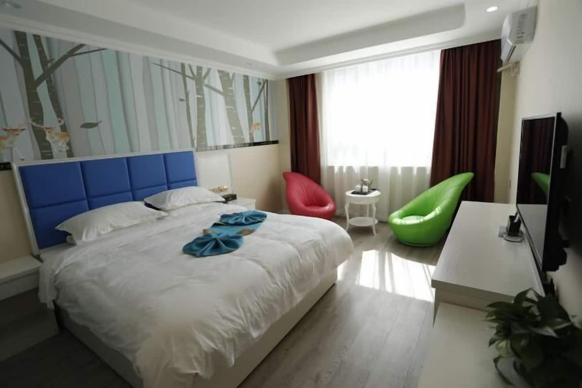 Ein Hotelzimmer mit einem großen Bett, einem Schreibtisch, einem Sessel, einem Fernseher und einem Fenster mit Vorhängen.