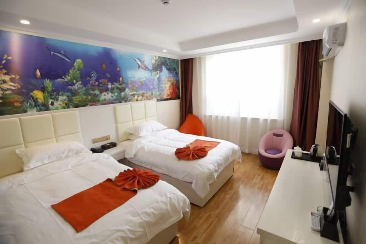 Ein Hotelzimmer mit zwei Betten, einem großen Wandgemälde mit Unterwasser-Motiv, einem Fenster mit Vorhängen und einem Schreibtisch mit Stuhl.