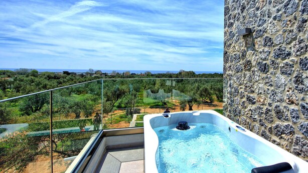 Un jacuzzi en un balcón con vistas a un risco y un paisaje con árboles y una masa de agua a lo lejos.