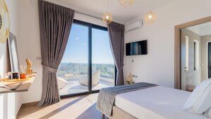 Un dormitorio moderno con una cama grande, un televisor montado en la pared y un balcón con vistas.