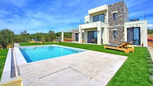 Una casa moderna de dos pisos con piscina, mobiliario exterior y fachada de piedra.