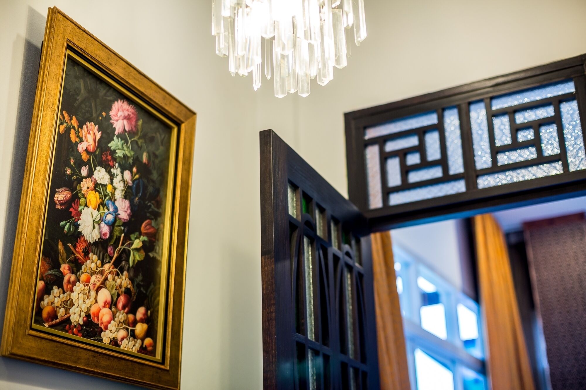 A framed floral painting on the wall, a decorative black metal gate, and a chandelier.