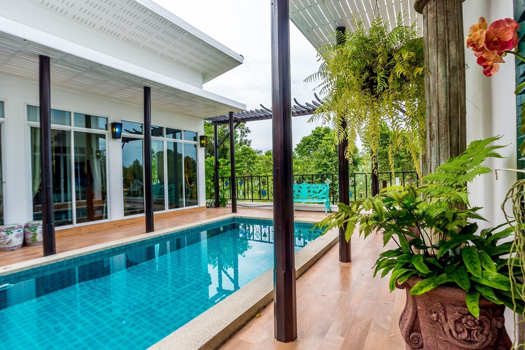 A modern pool area with a clear blue pool, a pergola with hanging plants, and a white building with large windows.