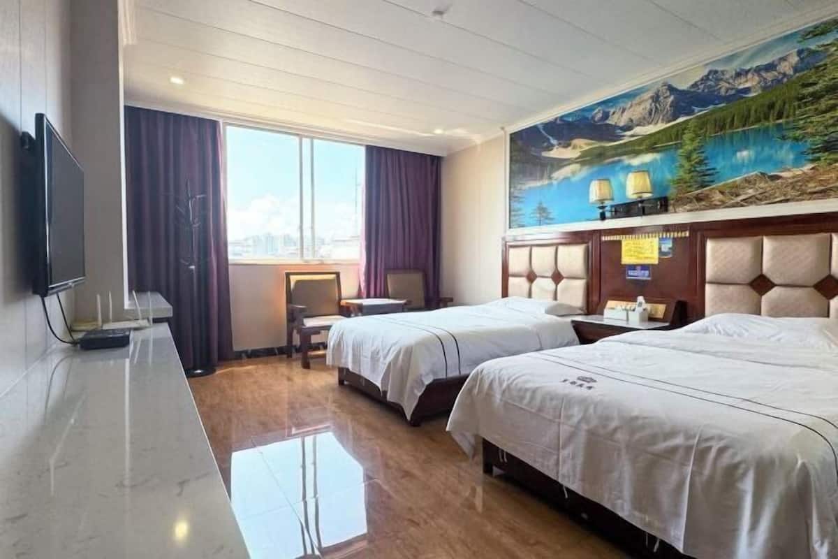 A hotel room with two beds, a TV, a desk, a chair, and a large window with curtains.
