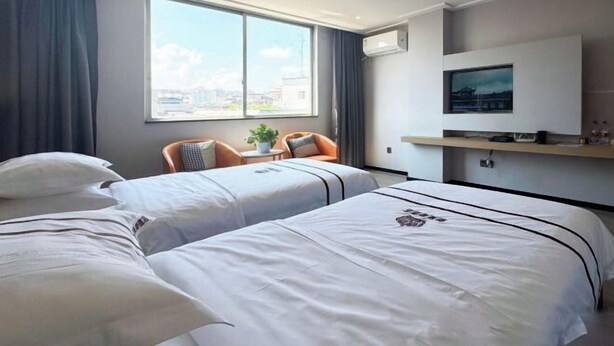 A hotel room with two beds, a TV, a window with a city view, and a small table with a plant. - Xinhuangdu Hotel, Xupu (Lipu)