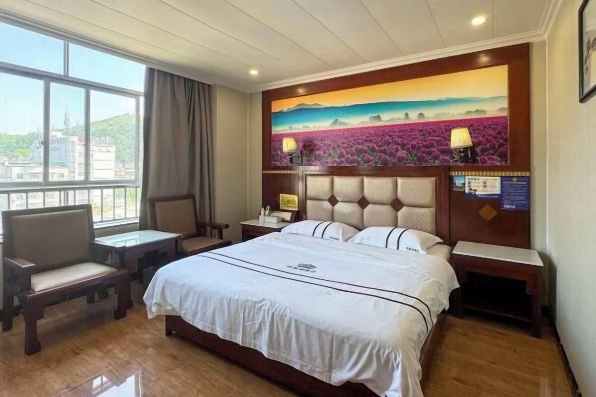 A hotel room with a bed, a desk, a chair, a nightstand, a lamp, and a painting on the wall.