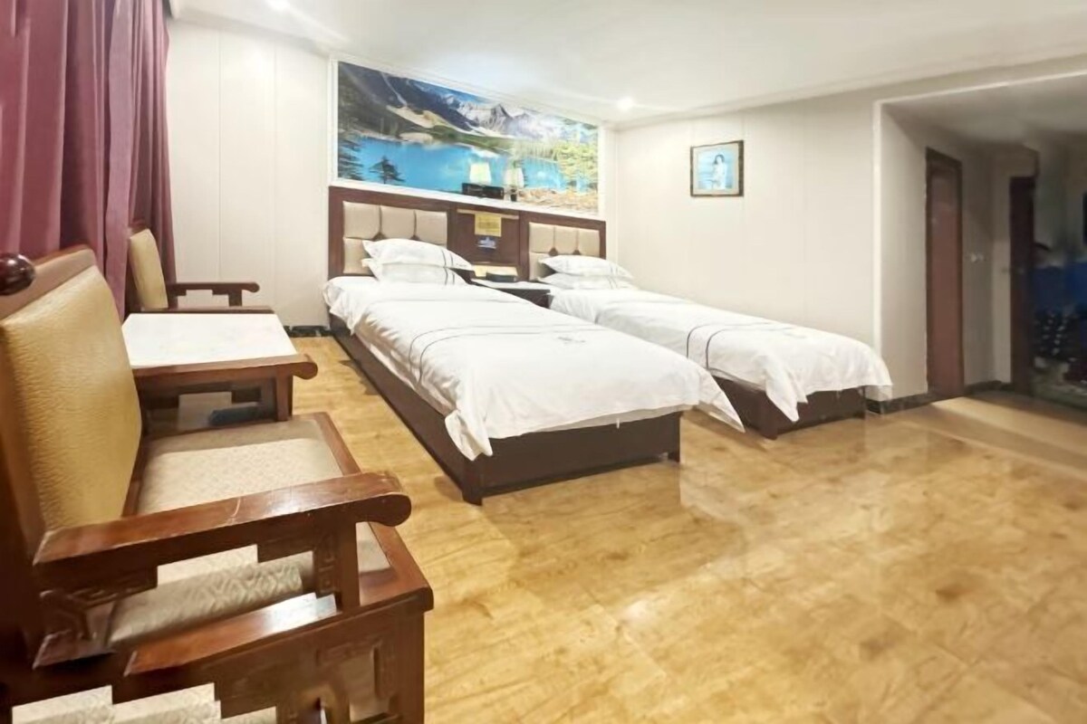 A hotel room with two beds, a wooden chair, a desk, and a painting on the wall.