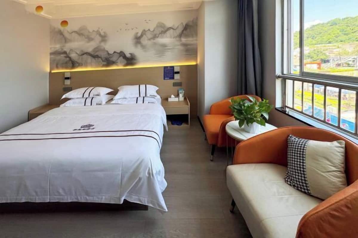 A hotel room with a bed, a sofa, a small table with a plant, and a window with a view of the outdoors.