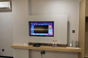 A television mounted on a wall in a hotel room, with a control panel and a water bottle on the shelf below. - Xinhuangdu Hotel, Xupu (Lipu)