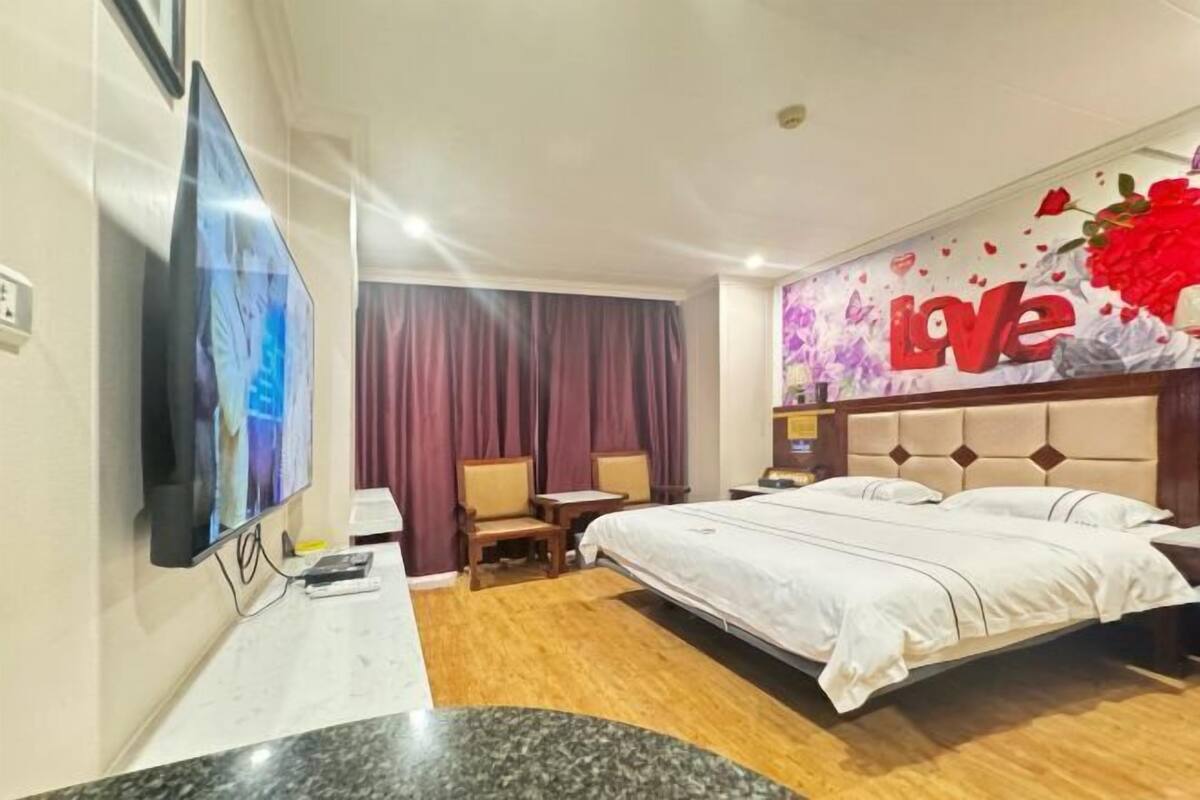 A hotel room with a bed, a TV, a desk, and a wall with a 'Love' decoration.