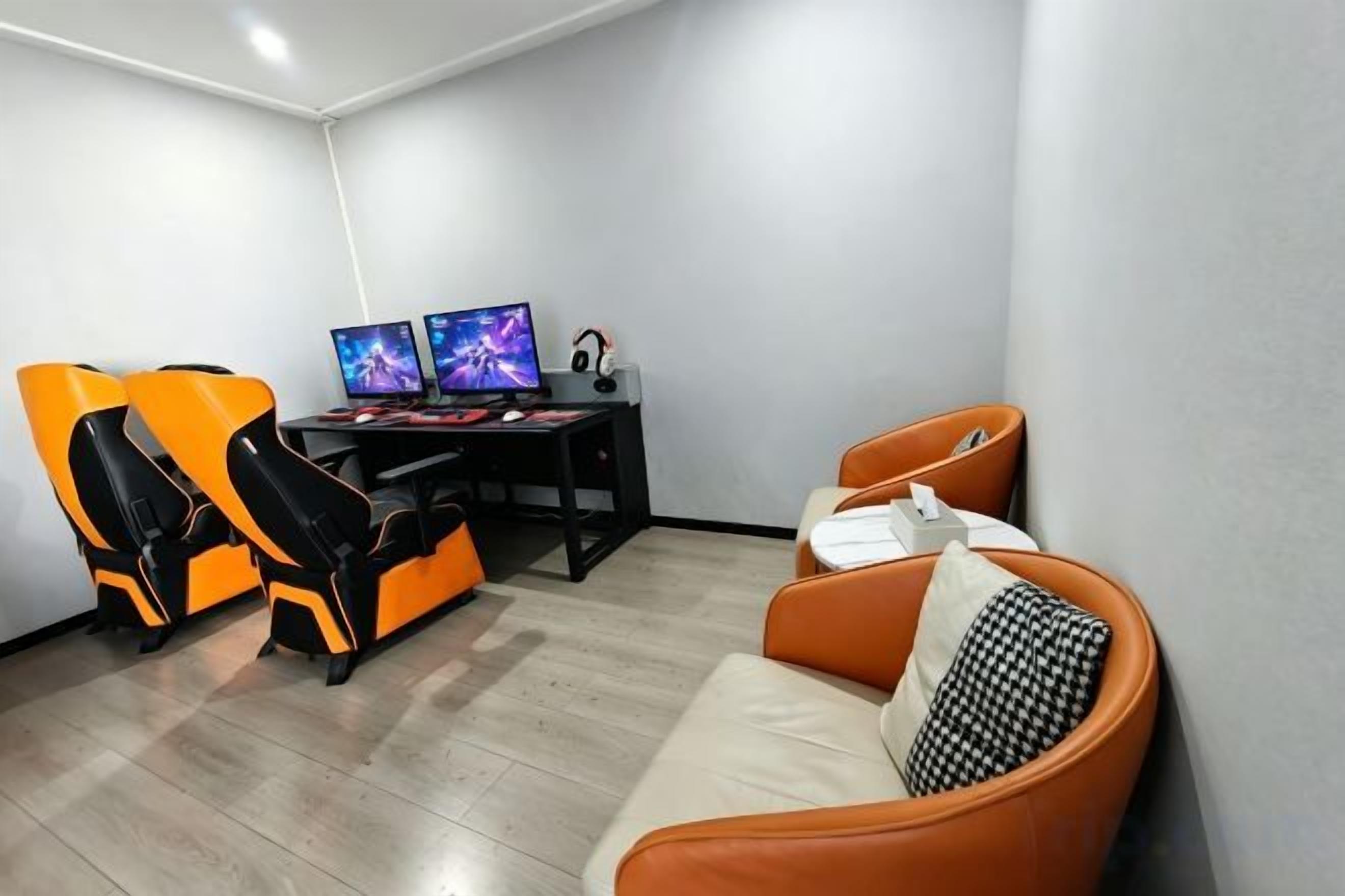 Een kamer met een gaming stoel, een bureau met twee monitoren en een bank.