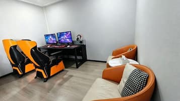Een kamer met een gaming stoel, een bureau met twee monitoren en een bank.