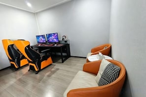 Een kamer met een gaming stoel, een bureau met twee monitoren en een bank.