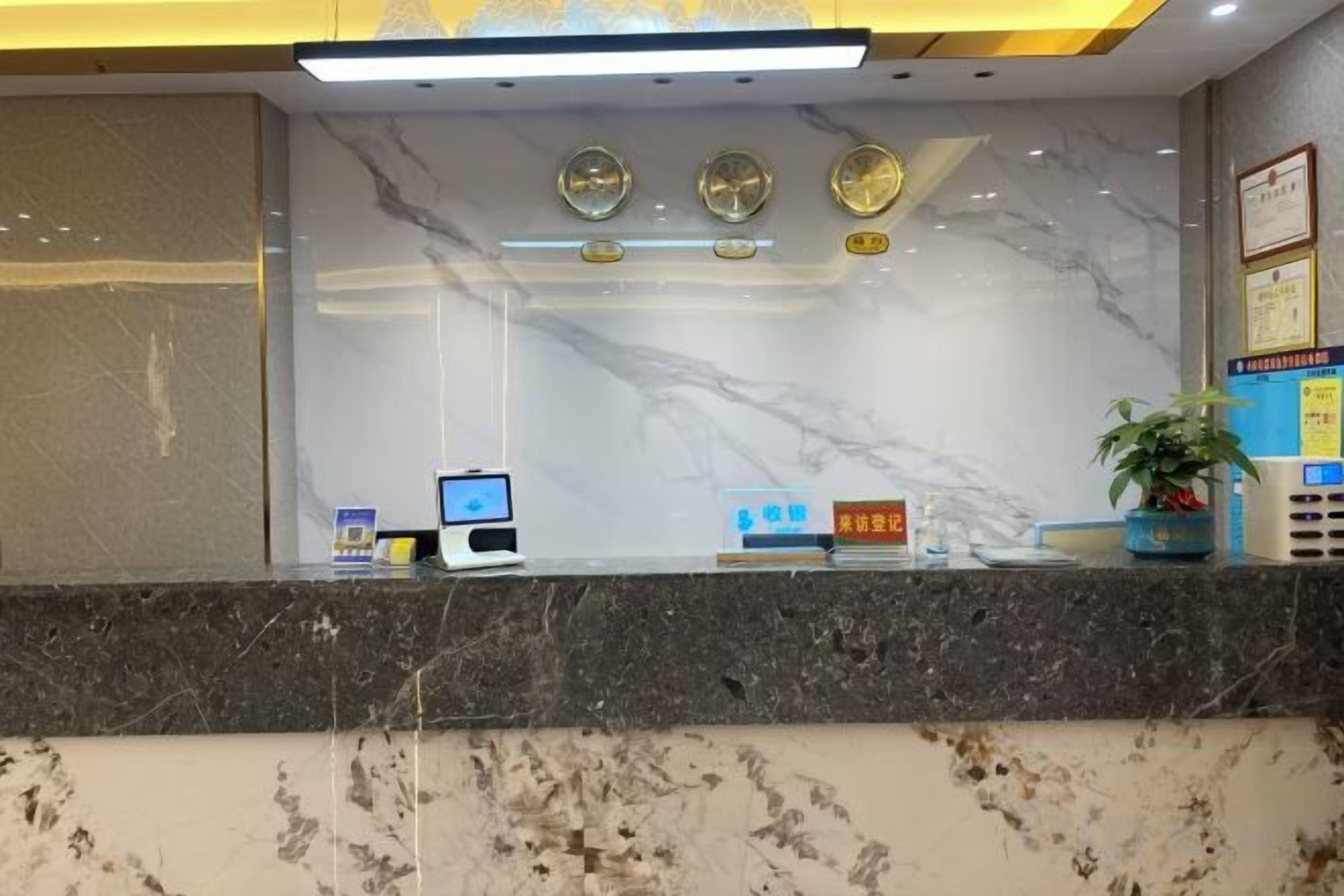 A reception desk with a marble wall, a plant, and a digital kiosk.