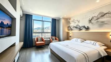 A hotel room with a large bed, a television, a desk with a chair, and a window with curtains.