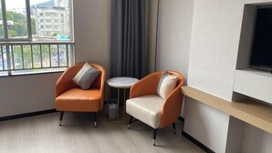 A hotel room with two armchairs, a small round table, a TV mounted on the wall, and a view of buildings outside. - Xinhuangdu Hotel, Xupu (Lipu)