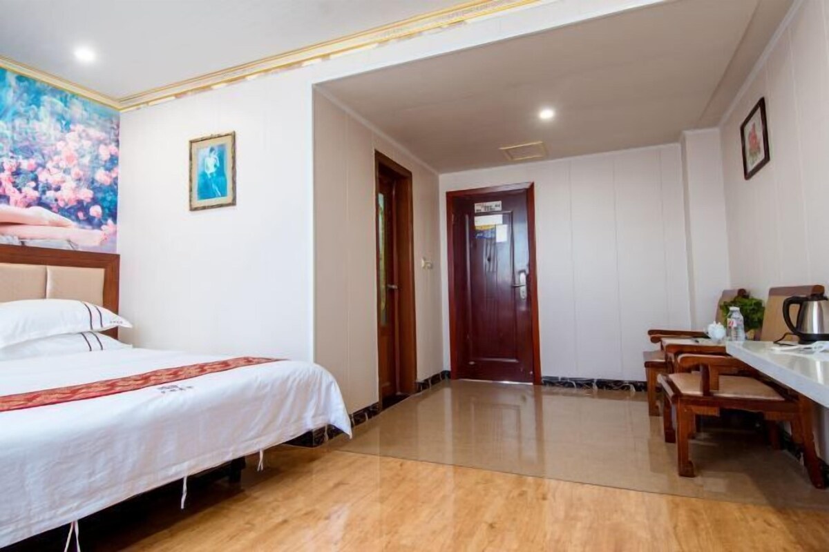 A hotel room with a bed, a dining table with chairs, a wooden door, and a painting on the wall.