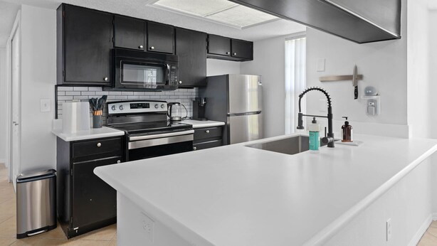 Une cuisine moderne avec des meubles noirs, des appareils en acier inoxydable et un îlot central blanc.