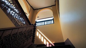 Una escala amb baranes de metall ornamentades i vista d'una habitació propera a través d'una finestra apuntada.