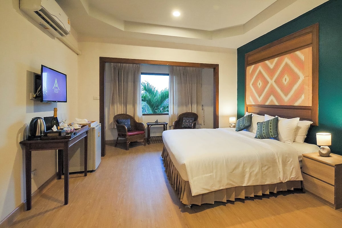Habitación de hotel con cama, escritorio con computadora, silla, televisor y ventana con cortinas.