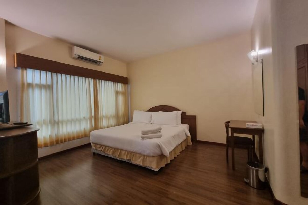 A hotel room with a bed, a desk, a chair, a TV, and an air conditioning unit.