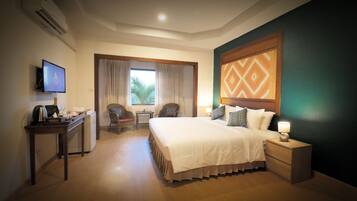 A hotel room with a bed, bedside table, TV, desk, chair, and a window with curtains.
