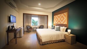 Habitación de hotel con cama, mesita de noche, televisión, escritorio, silla y ventana con cortinas.