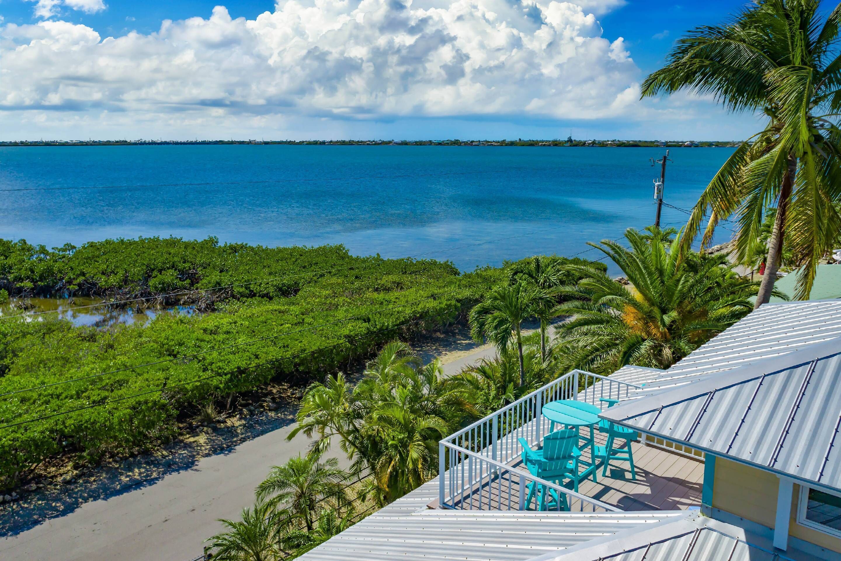 A coastal view with a balcony, palm trees, and a clear sky.