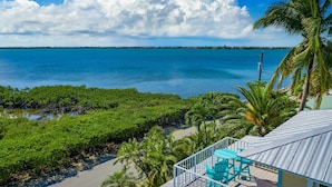 A coastal view with a balcony, palm trees, and a clear sky. - Slice of Paradise: Big Pine Key Waterfront | Heated Pool, Dockage & Open-Water Views (Big Pine Key)