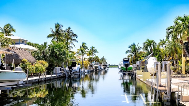 A canal with boats docked, surrounded by palm trees and a clear sky. - Slice of Paradise: Big Pine Key Waterfront | Heated Pool, Dockage & Open-Water Views (Big Pine Key)