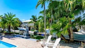 A poolside area with lounge chairs, a boat dock, and a building in the background. - Slice of Paradise: Big Pine Key Waterfront | Heated Pool, Dockage & Open-Water Views (Big Pine Key)