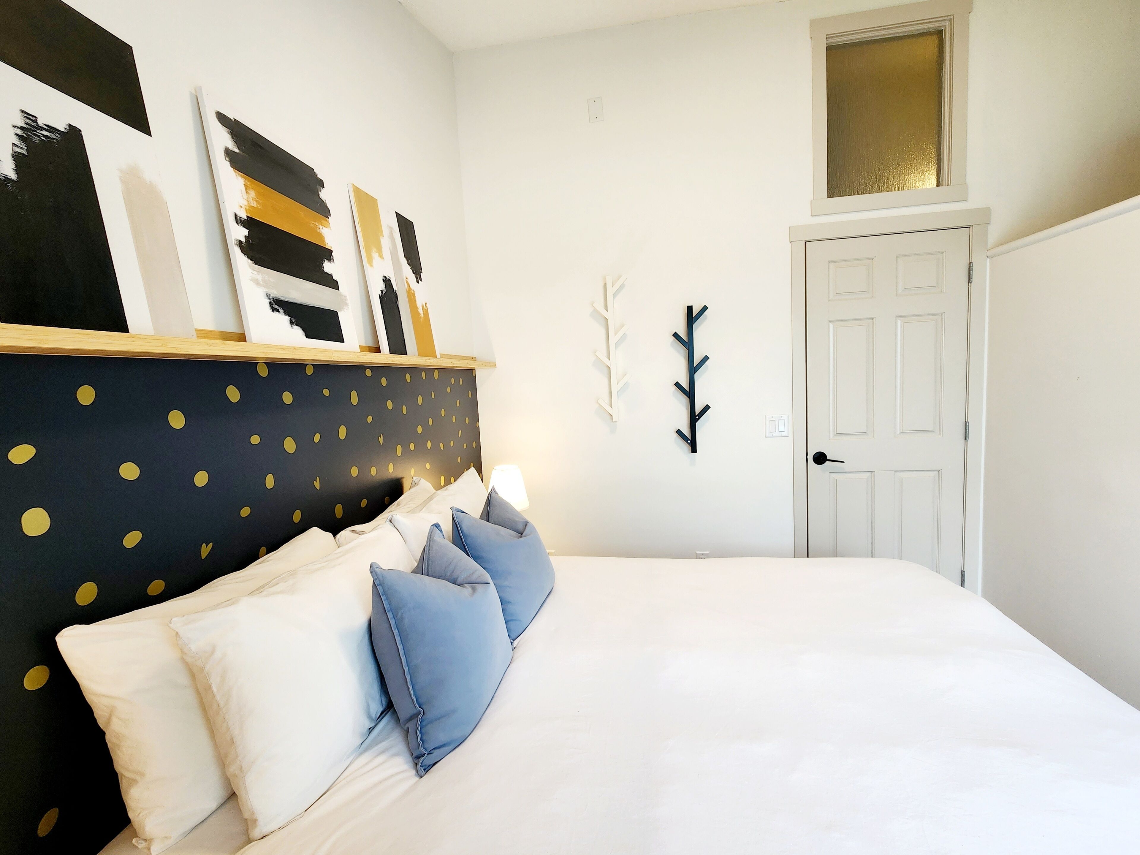 Un dormitorio con cama, paredes blancas, una puerta y una ventana.