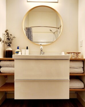 A bathroom with a round mirror, a sink, and shelves with towels.